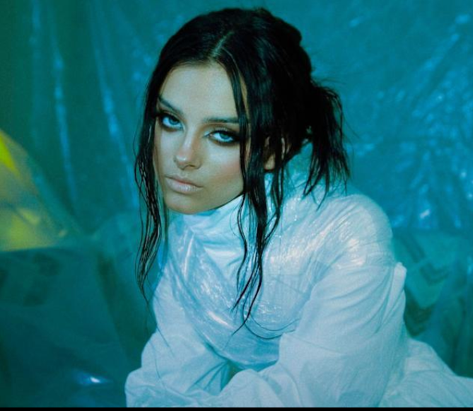 Female music artist portrait with dark hair against a blue background